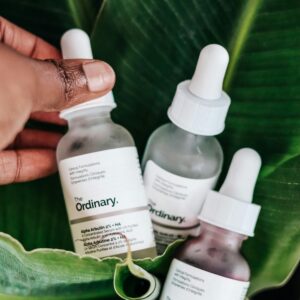 Close-up of skincare bottles on bright green leaves with human hand, emphasizing natural beauty ingredients.
