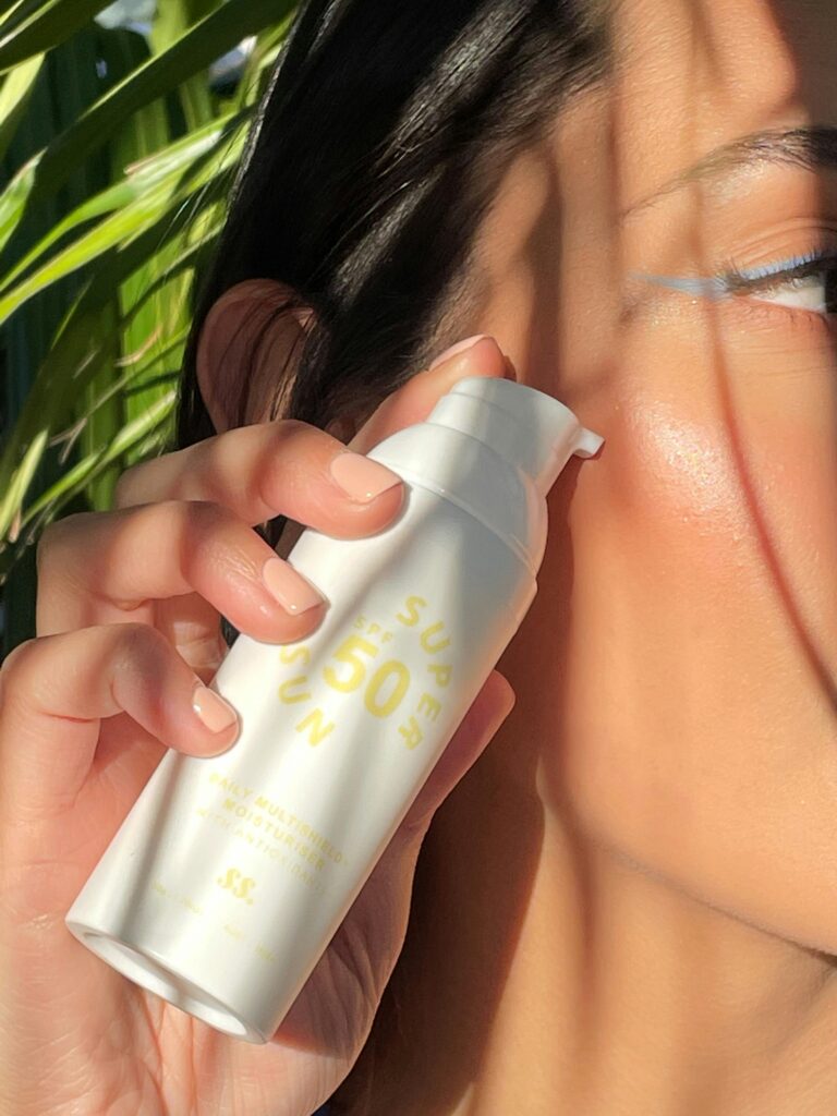 Close-up of a woman applying SPF 50 sunscreen with natural sunlight and greenery.